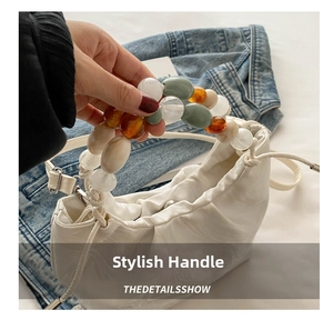Detail of white cloud pleated bag featuring a colorful beaded handle and drawstring closure
