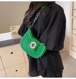 Detail of green crescent bag featuring a luxury crystal buckle and metal chain strap