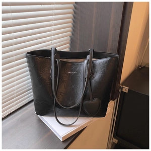 Detail of black leather tote bag with heart charm and brand logo on book stack