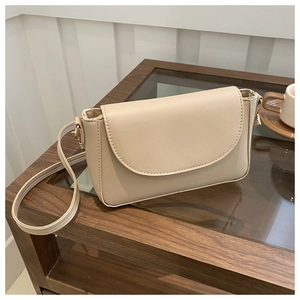Detail of a beige PU leather crossbody bag with a curved flap and gold metal hardware