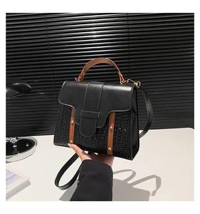 Detail of a chic handbag featuring black crocodile pattern leather and brown strap accents