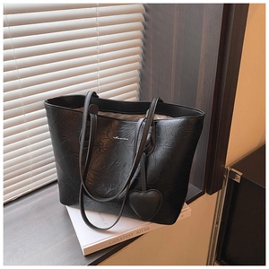 Close-up of black pleated leather tote bag with heart pendant on a book background