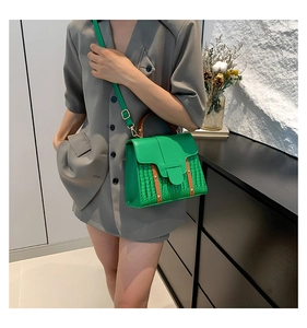 Detail of green faux crocodile leather bag with gold hardware worn by model