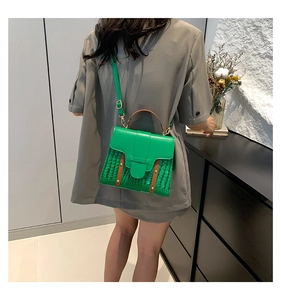 Detail of green crocodile pattern handbag with brown handles worn by a model