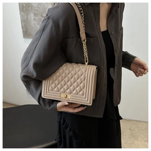 Detail of beige quilted shoulder bag with metal chain strap and rectangular lock closure