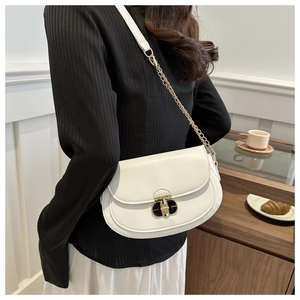 Detail of white saddle bag with gold chain strap and metal buckle worn by a model