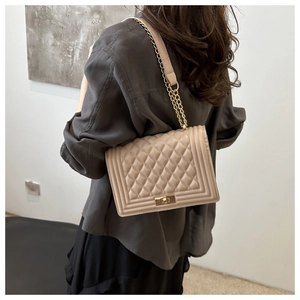 Detail of beige quilted shoulder bag with golden twist lock and chain strap on model