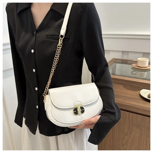 Detail of white saddle bag featuring gold clasp and chain strap worn by a model