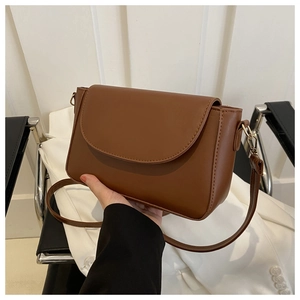 Detail of caramel brown PU leather crossbody bag with curved flap and gold metal hooks