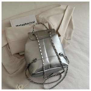 Detail view of silver metallic backpack with chain straps on a beige background