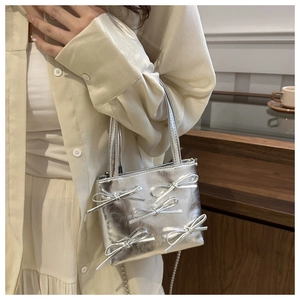 Close-up of silver bow accents and metallic texture on a minimalist fashion handbag
