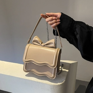 Beige crossbody bag with wavy flap and bow detail, including chain and leather straps