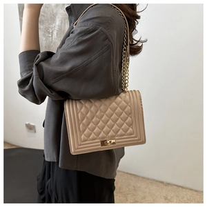 Detail of beige quilted shoulder bag with golden chain strap and metal lock closure