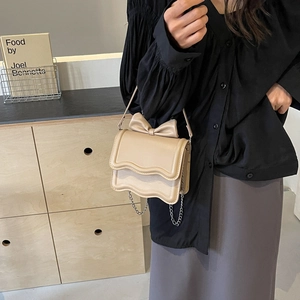 Beige crossbody bag with wavy flap design and elegant bow detail shown on a model