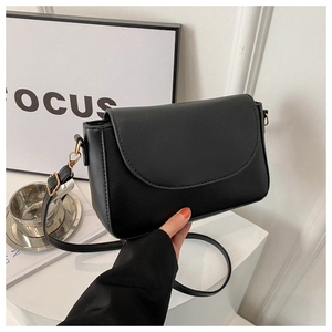 Detail of minimalist black leather crossbody bag with flap cover and gold metal buckle