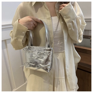 Detail of silver metallic bucket bag featuring 3D bows and a bead chain strap