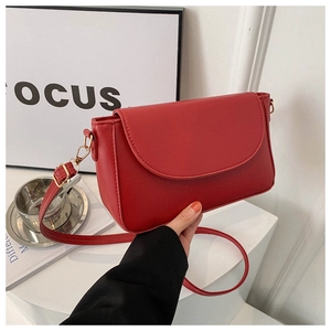Detail view of red leather crossbody bag with rounded flap and slim shoulder strap