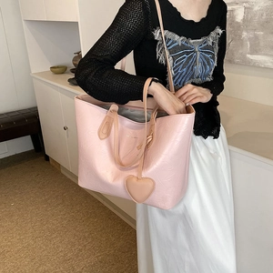 Pink PU tote bag with textured finish and heart charm shown on model's shoulder