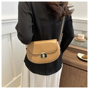 Detail of camel leather saddle bag with gold chain strap and metal double-ring clasp
