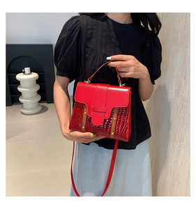 Detail of red crocodile texture handbag with decorative strap and metallic hardware