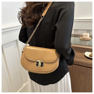 Detail of camel saddle bag featuring a gold metal twist lock and leather chain strap