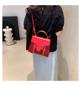 Détail du sac à main bicolore rouge et marron effet crocodile porté à l'épaule
