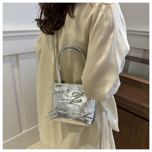Silver metallic bow bucket bag with chain strap shown on a model from a side angle