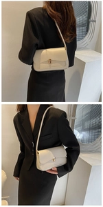 Detail of minimalist cream baguette bag with gold square buckle worn under the arm