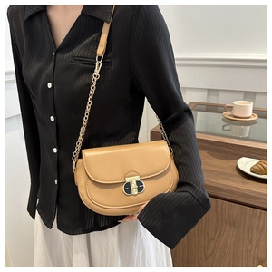 Detail of khaki crossbody bag with oval metal clasp and gold chain strap on model