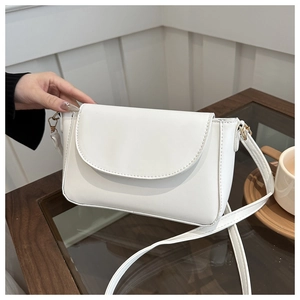 Close-up of stylish white crossbody bag with gold hardware on a wooden table setup