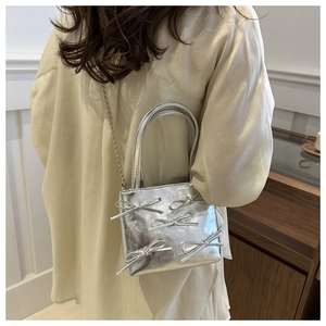 Detail of silver metallic bow handbag with bead chain strap worn by a model