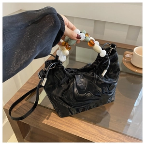 Detail of glossy black pleated bucket bag with colorful marble beaded handle
