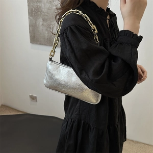 Sac baguette argenté métallisé avec bandoulière chaîne dorée sur une robe noire