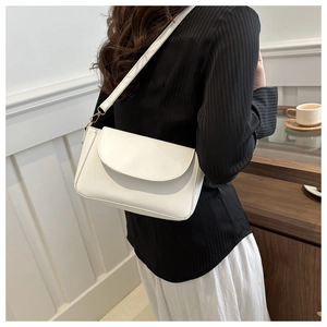 Detailed view of a minimalist white leather crossbody bag worn with a chic pleated top