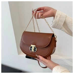 Detailed view of brown leather saddle bag featuring gold chain and oval twist lock clasp