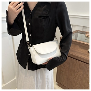 Close-up of a white minimalist flap shoulder bag worn with a chic black striped shirt