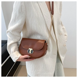 Detail of a brown leather saddle bag featuring a gold twist lock and a chain strap