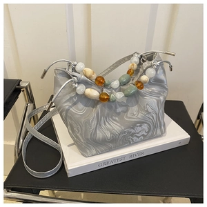 Detail of silver marble bucket bag featuring colorful beaded handle and metal strap