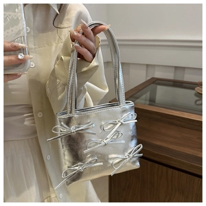 Detail of silver metallic handbag featuring 3D bow accents and a slim shoulder strap