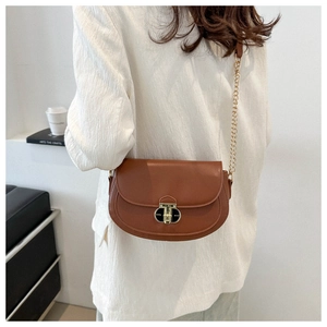Detail of a brown saddle bag featuring a gold semi-circular lock and fine chain strap