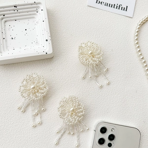 Detailed close-up of beaded pearl flower phone grip with dangling tassels on white base