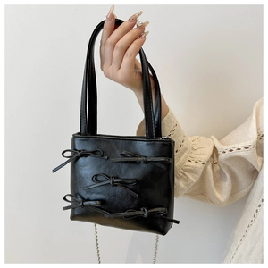 Detail of a black bow-knot mini tote bag with stylish bead chain and leather texture