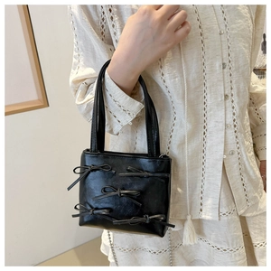 Detail of a black bucket bag with leather bows and delicate metal ball chain strap