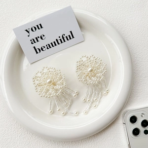 Macro shot of white beaded flower earrings with pearl tassels on a ceramic tray