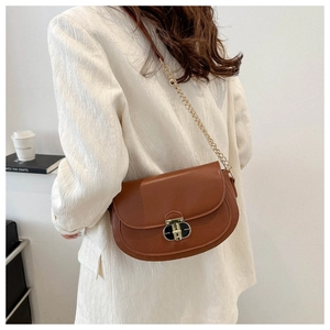 Detail of caramel brown saddle bag with metal clasp and chain strap on a model