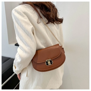 Close-up of brown saddle bag with golden double-ring lock and chain strap on white blazer