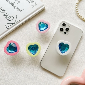 Detail of heart-shaped phone grip with a blue multi-faceted gemstone on a white surface