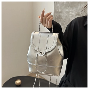 Close-up of a mini silver metallic backpack with chain straps and woven top handle