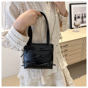 Detail of a black crossbody bag featuring elegant bows and a beaded metal chain strap