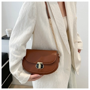 Detail of a brown saddle bag featuring a gold twist lock and chain strap on a blazer